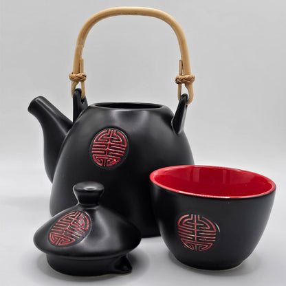 A black and red ceramic tea set, a teapot with a bamboo handle, and four cups, black outside and red inside with a red kanji symbol.