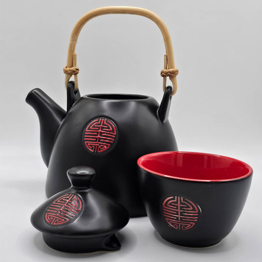 A black and red ceramic tea set, a teapot with a bamboo handle, and four cups, black outside and red inside with a red kanji symbol.